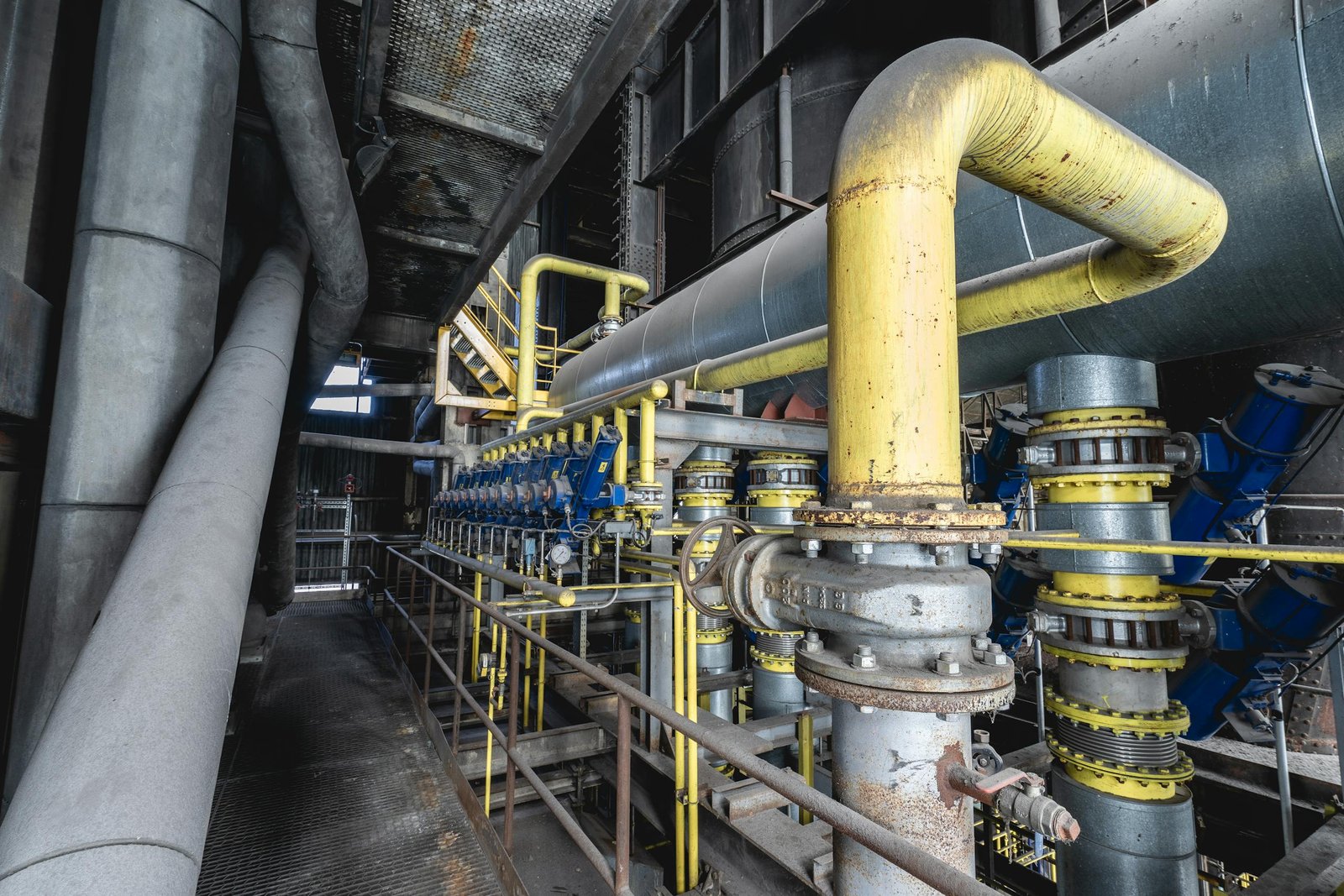 Close-up of an intricate industrial pipeline system featuring yellow valves and steel structures inside a factory.