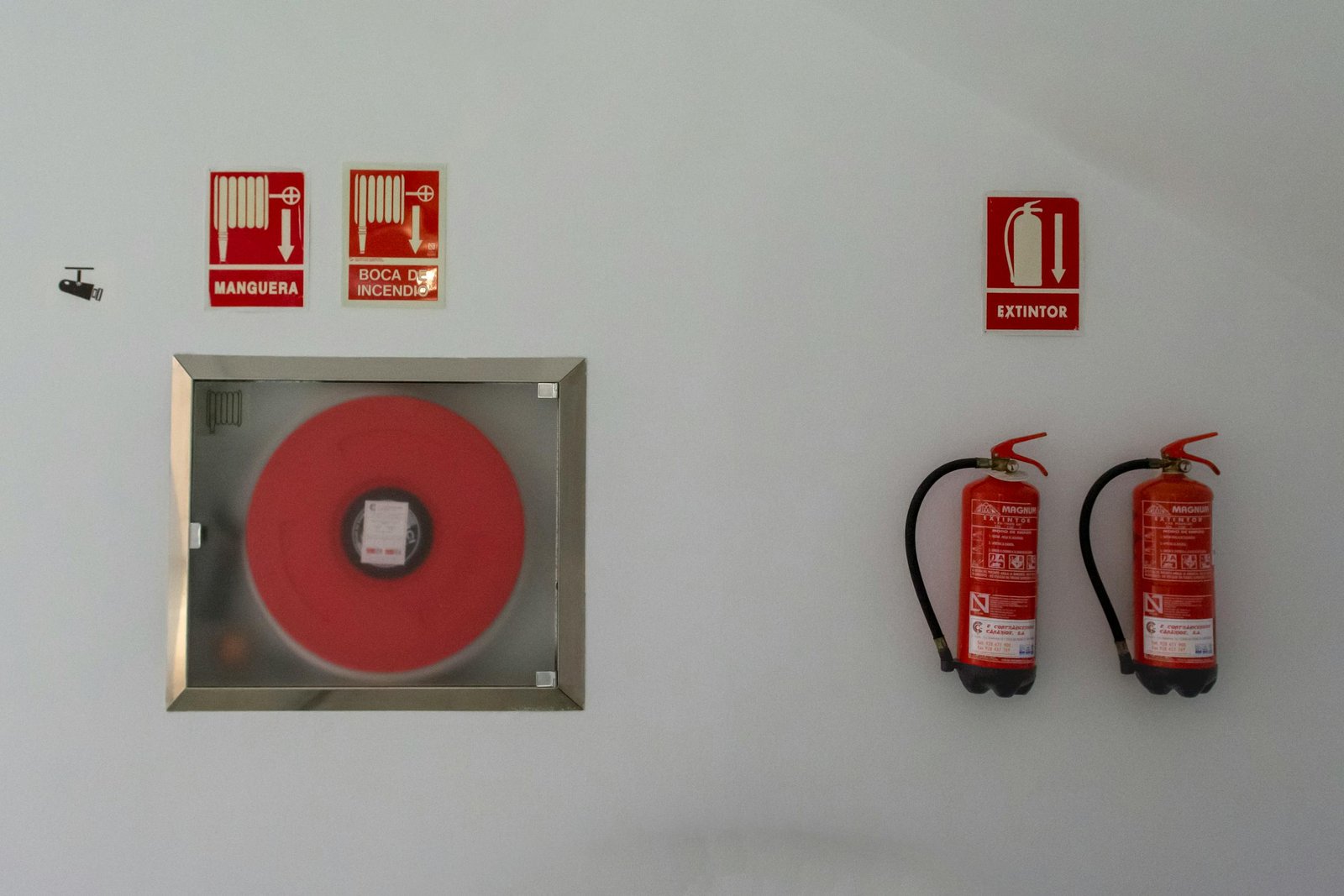 Fire safety setup with extinguishers and hose reel on a white wall for emergency preparedness.